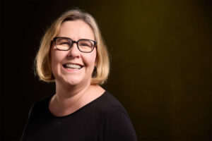 Portrait photo of Emma smiling on a dark background.