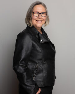 Emma standing with hands in her pockets wearing a black leather jacket.