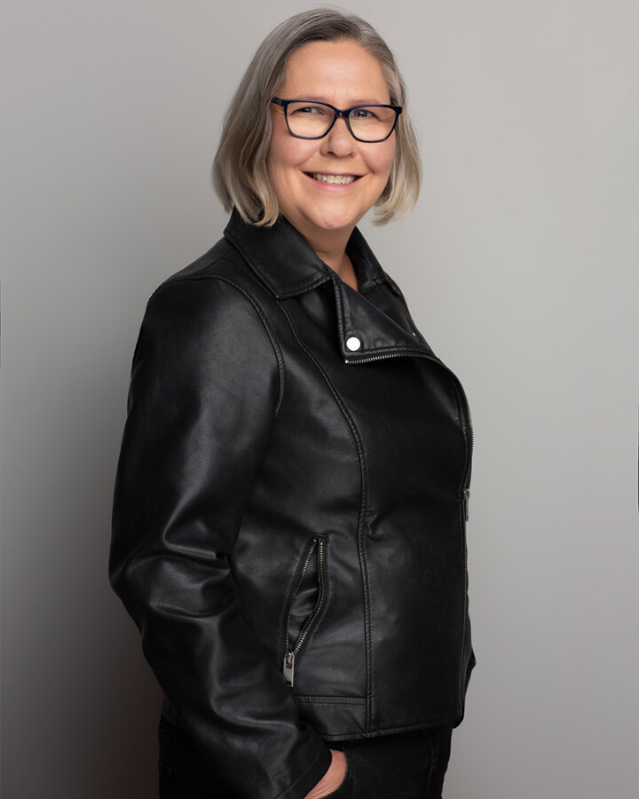 Emma standing with hands in her pockets wearing a black leather jacket.