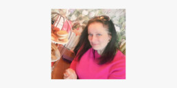 Julie wearing a pink jumper eating afternoon tea.