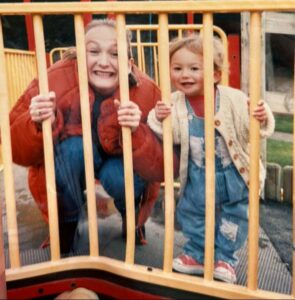 Sarah Hussey and Holly as a child looking through playground bars.